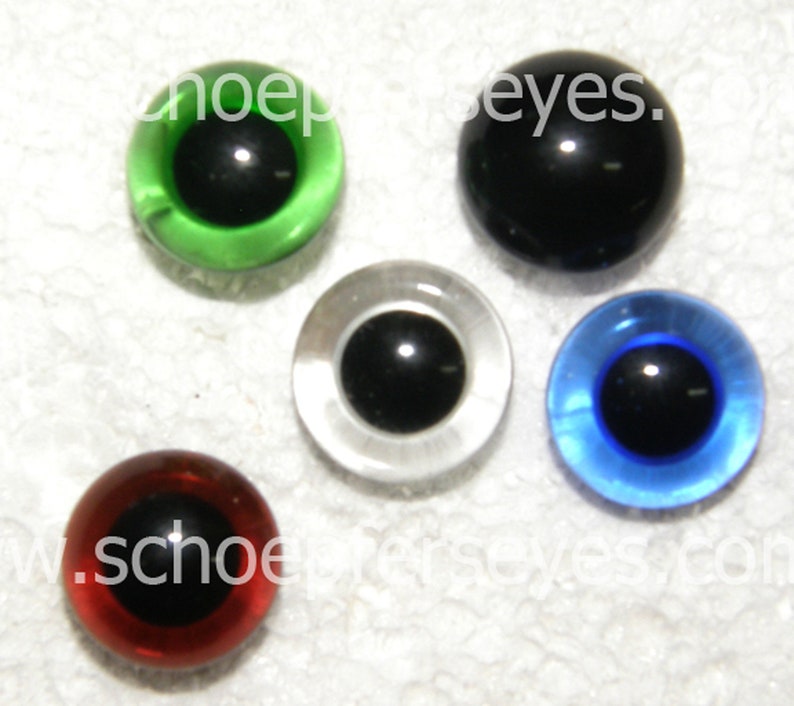 May include: Five different colored plastic googly eyes with black pupils. The colors are green, black, clear, blue, and red.