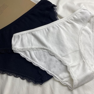 Puede incluir: Un par de braguitas de corte alto en negro sólido y blanco sólido, ambas con una sutil textura de patrón de diamantes y un delicado borde de encaje festoneado a lo largo de las aberturas de las piernas y la cintura para un aspecto refinado.