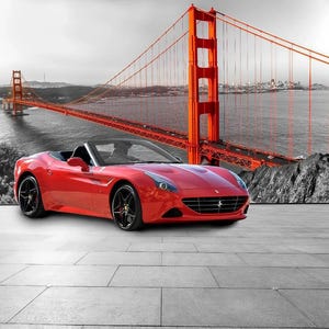 Può includere: Un'auto sportiva decappottabile rosso brillante con ruote nere parcheggiata su una superficie piastrellata grigia. Lo sfondo presenta una fotografia in bianco e nero ad alto contrasto del Golden Gate Bridge con la sua struttura.
