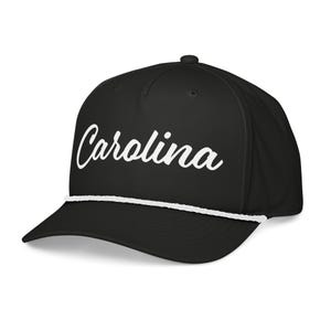 Puede incluir: Gorra de béisbol negra con la palabra "Carolina" en escritura blanca en la parte delantera. La gorra tiene un detalle de cuerda blanca a lo largo del borde.