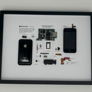 Peut inclure: Cadre artistique présentant une vue éclatée d'un iPhone 3G, avec ses composants disposés autour d'un téléphone noir. Le texte "iPhone 3G" est en haut, avec des détails techniques. Le cadre est noir.