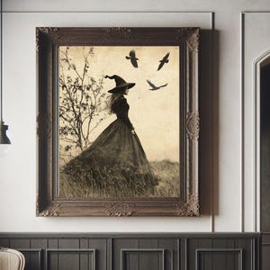 May include: A framed sepia-toned print depicts a figure in a witch's hat and gown, standing in a field with crows overhead. The ornate, dark wood frame complements the gothic aesthetic. The artwork hangs on a dark paneled wall.