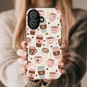 May include: A phone case featuring a repeating pattern of coffee cups, to-go cups, and coffee beans in shades of brown, pink, and white. The case has a light beige background and a black camera lens cutout.