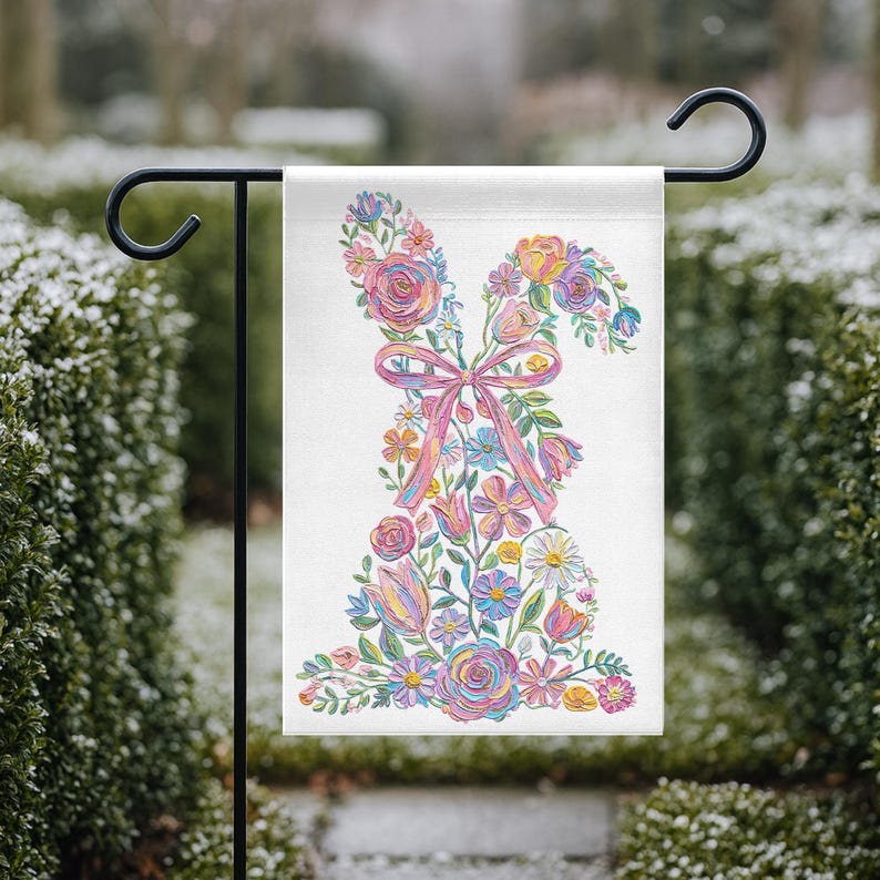 May include: A garden flag with a floral bunny design. The bunny is made of colorful flowers, including roses and tulips, with a pink bow. The flag is displayed on a black metal stand, ideal for spring or Easter.
