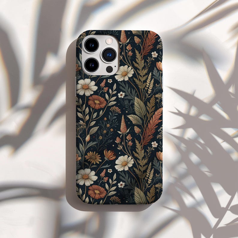 K&ouml;nnte beinhalten: Eine Smartphone-H&uuml;lle mit dunkelblauem Hintergrund und einem dichten botanischen Muster aus wei&szlig;en G&auml;nsebl&uuml;mchen, rostfarbenen Bl&uuml;ten sowie verschiedenen gr&uuml;nen und braunen Bl&auml;ttern. Die H&uuml;lle verf&uuml;gt &uuml;ber einen Ausschnitt f&uuml;r ein Dreifach-Kamerasystem.