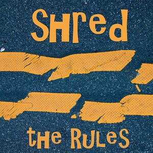 May include: A close-up of a cracked yellow road marking with the words "Shred the Rules" painted in orange on a dark asphalt surface.