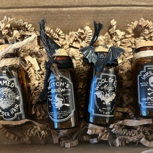 May include: Four small, brown glass bottles with cork stoppers, each labeled with spooky Halloween-themed text and graphics. The bottles are filled with liquid and decorated with twine and black accents, presented in a cardboard box with shredded paper.