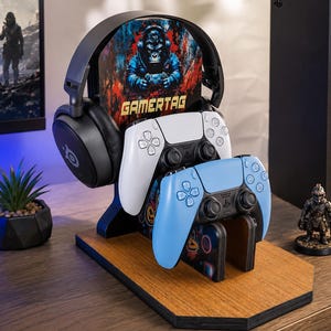 May include: A wooden gaming stand featuring a black headset, a white controller, and a light blue controller. The stand has a central panel with a graphic of a gorilla wearing headphones and the text GAMERTAG printed in yellow block letters.
