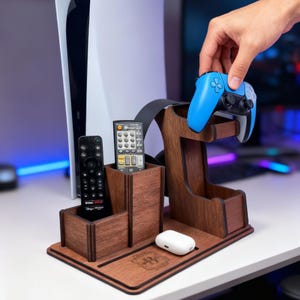 May include: A wooden desk organiser with compartments for remotes, a headset, and a blue game controller. The organiser also has a small tray for accessories. The wood has a dark brown finish.
