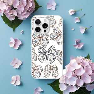 May include: White phone case with a repeating pattern of blue and brown bows. The bows have a floral design. The case is surrounded by pink and purple flowers on a light blue background.