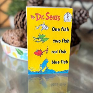 May include: A yellow book cover with the title "One Fish, Two Fish, Red Fish, Blue Fish" by Dr. Seuss. The cover features illustrations of fish in white, green, red, and blue. The book is a "Beginner Book".