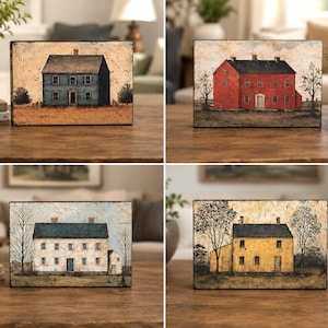 Four primitive Americana decor blocks displayed together on a wooden table in an elegant living room, featuring vintage colonial saltbox homes in distressed blue, red, cream, and mustard tones with early American farmhouse style.