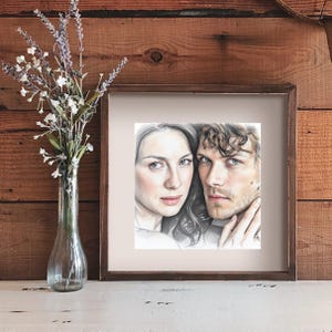 May include: A framed pencil sketch portrait of a man and woman. The woman has long hair and is looking at the viewer. The man has curly hair and is touching the woman's face. A vase of flowers is to the left.