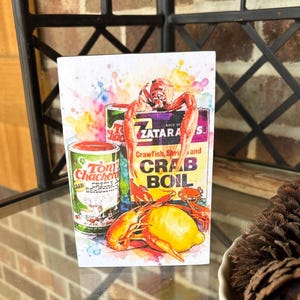 May include: Watercolor-style wood block featuring Tony Chachere's Creole Seasoning and Zatarain's Crab Boil boxes, with crawfish and a lemon. The image includes text: "Crawfish, Shrimp and Crab Boil". The seasoning can reads "Net Wt. 6 oz. 227 grams".