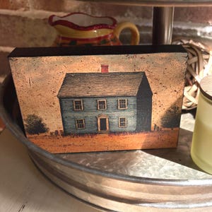 Primitive country decor block with blue colonial farmhouse artwork, distressed vintage finish, and rustic Americana style displayed on a tiered tray.