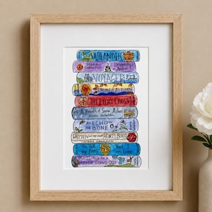 May include: A framed watercolor illustration of a stack of books by Diana Gabaldon. The spines are labeled Outlander, Dragonfly in Amber, Voyager, Drums of Autumn, The Fiery Cross, A Breath of Snow Ashes, An Echo in the Bone, Written in My Own Heart's Blood, Go Tell the Bees That I am Gone, and A Blessing for a Warrior Going Out.