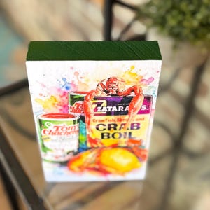 May include: Watercolor-style wood block featuring Tony Chachere's Creole Seasoning and Zatarain's Crab Boil boxes, with crawfish and a lemon. The image includes text: "Crawfish, Shrimp and Crab Boil". The seasoning can reads "Net Wt. 6 oz. 227 grams".