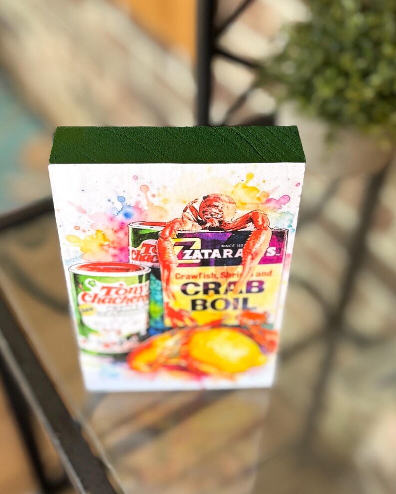 May include: Watercolor-style wood block featuring Tony Chachere's Creole Seasoning and Zatarain's Crab Boil boxes, with crawfish and a lemon. The image includes text: "Crawfish, Shrimp and Crab Boil". The seasoning can reads "Net Wt. 6 oz. 227 grams".