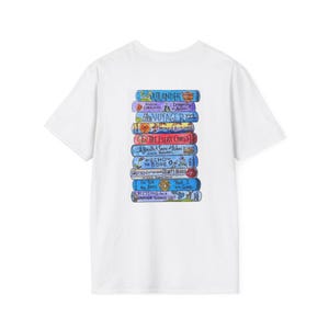 May include: White t-shirt with a print of a stack of books. The book titles include "Outlander" and "Voyager." The spines are blue, purple, and orange, with white lettering. The t-shirt has a round neck.