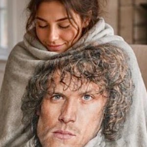 Puede incluir: Una mujer y un hombre están envueltos en una suave manta gris. El hombre tiene el pelo rizado castaño y ojos azules. La mujer tiene el pelo castaño y está mirando hacia abajo. La manta parece estar hecha de un material suave y tejido.