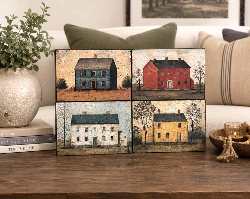 Four primitive Americana decor blocks displayed together on a wooden table in an elegant living room, featuring vintage colonial saltbox homes in distressed blue, red, cream, and mustard tones with early American farmhouse style.