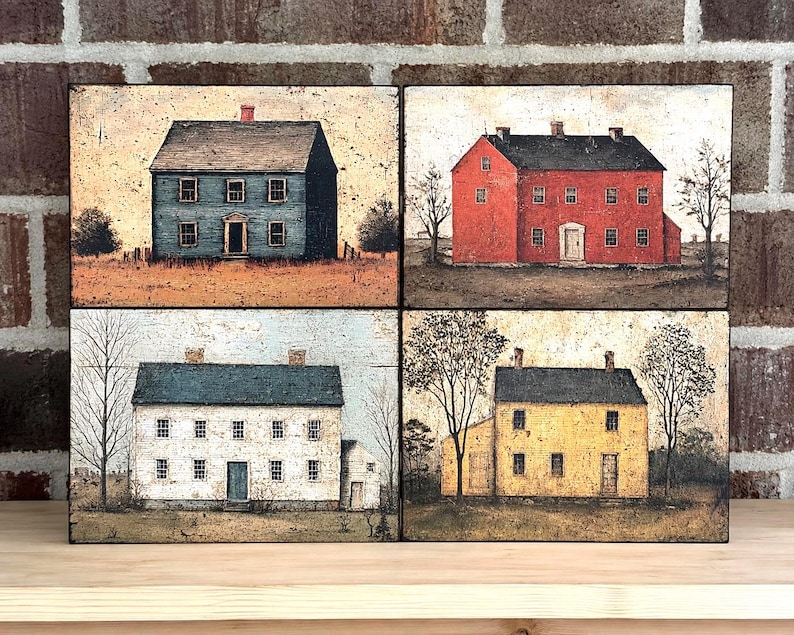 Four primitive Americana decor blocks displayed together on a wooden shelf against a rustic brick wall, featuring vintage colonial saltbox homes in distressed blue, red, cream, and mustard tones with early American farmhouse style.