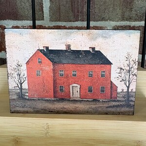 Rustic farmhouse decor block with vintage red colonial home artwork in distressed primitive style, displayed on a wood shelf with weathered Americana charm.