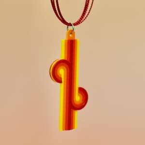 May include: A retro-style pendant necklace with a vertical, striped design in shades of yellow, orange, and red. The pendant is suspended from a series of thin, dark red cords. The necklace has a simple, yet eye-catching design.