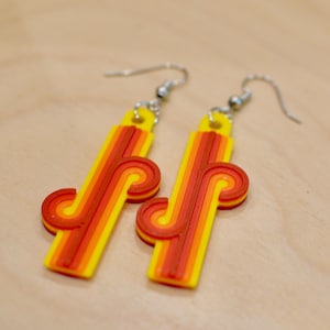 May include: A pair of retro earrings. Each earring has a yellow rectangular base with orange and red stripes and a curved design. They have silver-coloured hooks.
