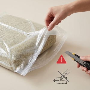 May include: A beige rectangular cushion is sealed in a clear plastic bag. A hand is pulling the bag open. A utility knife with a yellow accent is held near the bag, with a red warning sign and a no-cut symbol.