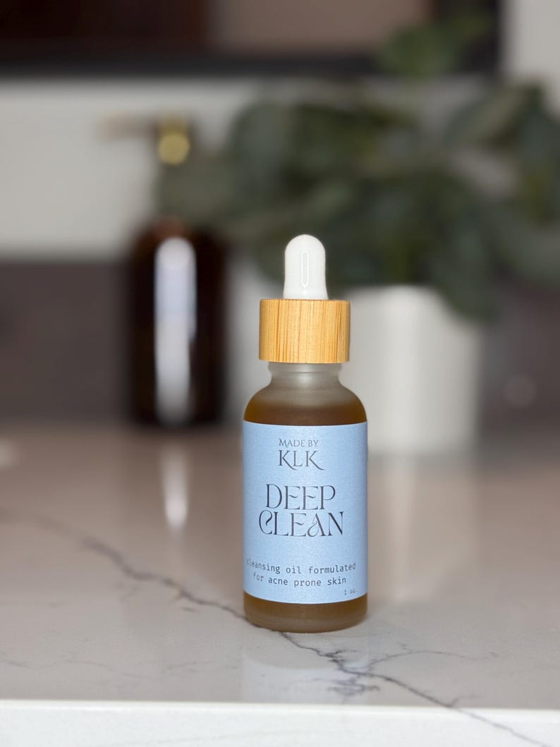 Puede incluir: Una peque&ntilde;a botella de vidrio transparente con tapa de madera y cuentagotas blanco. La etiqueta dice "DEEP CLEAN" y "cleansing oil formulated for acne prone skin". La botella contiene un l&iacute;quido dorado. La marca es "KLK".
