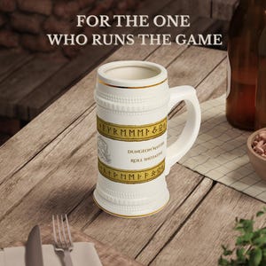 May include: White ceramic beer stein with a handle, featuring gold trim and a banner that reads "DUNGEON MASTER ROLL INITIATIVE." The stein has the text "FOR THE ONE WHO RUNS THE GAME" at the top. A perfect gift for tabletop gamers.