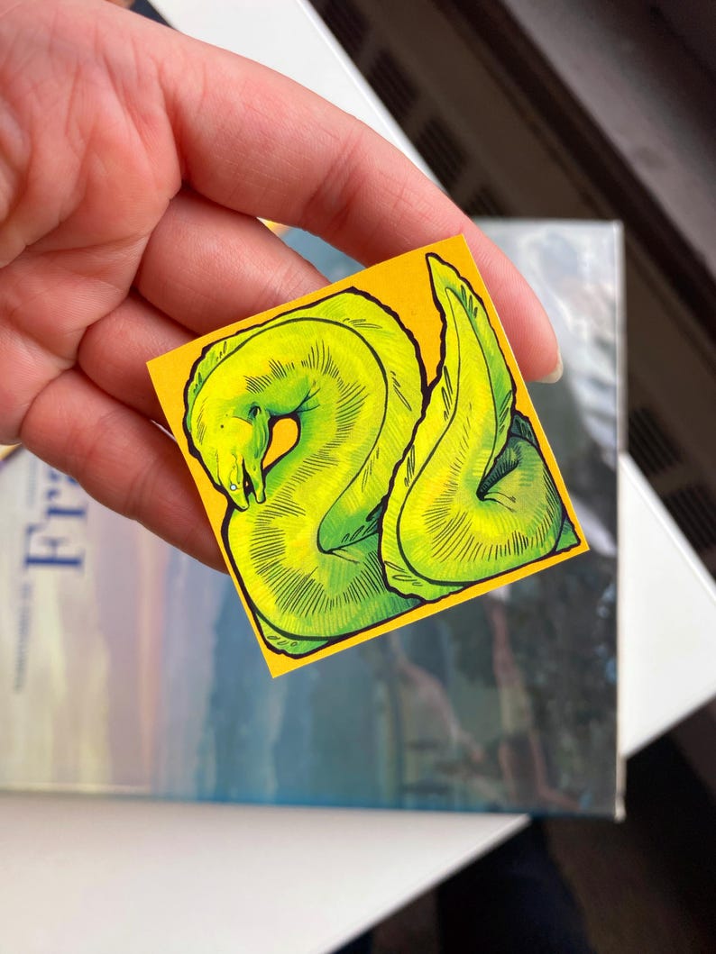 May include: A small, square sticker with a vibrant yellow background featuring a detailed illustration of a green moray eel. The eel is depicted in a stylized, artistic manner with dark green outlines and shading.
