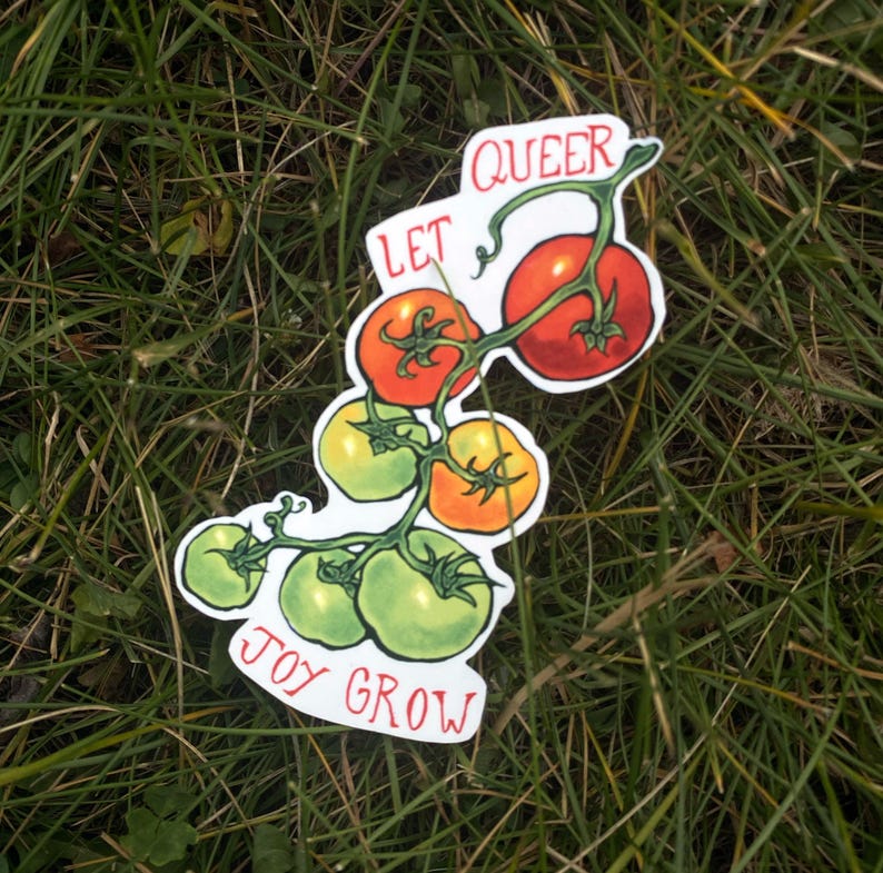 May include: A sticker depicting a sprig of tomatoes, some green, some orange, and some red. The sticker has the words "QUEER" and "LET JOY GROW" in red lettering. The sticker is set against a backdrop of green grass.