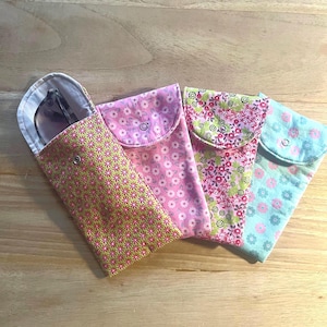 Op de afbeelding: Vier stoffen etuis voor brillen, elk met een eigen bloemenpatroon. De eerste is limoengroen met kleine roze bloemen, de tweede is lichtroze met witte bloemen, de derde heeft een dichte bloemenprint en de vierde is lichtblauw met roze bloemen.