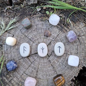 May include: A collection of crystals and runes arranged in a circle on a tree stump. The crystals include amethyst, rose quartz, tiger's eye, clear quartz, and sodalite. The runes are F, Y, and T.