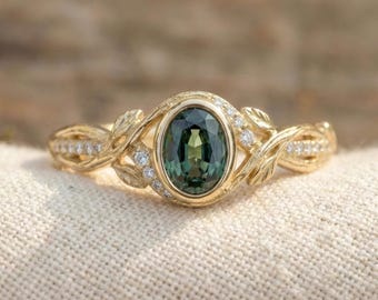 May include: A gold ring featuring an oval-cut dark green gemstone set in a bezel. The band is designed with textured, leaf-like metalwork and small, round, clear accent stones embedded along the sides of the shank, creating a botanical aesthetic.