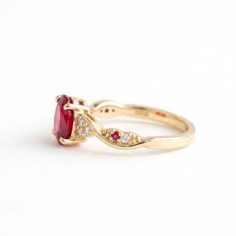 May include: A gold ring featuring a large oval-cut red gemstone as the centrepiece. The band has a twisted design accented with smaller round-cut white diamonds and tiny red gemstones embedded along the sides of the gold metal shank.