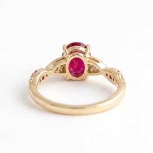 May include: A gold ring featuring a central oval-cut vibrant red gemstone held by a multi-prong setting. The band displays a twisted design with small accent stones embedded along the shoulders, showcasing a polished metallic finish throughout.