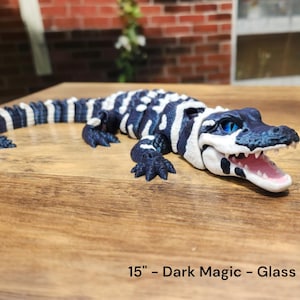 Peut inclure: Figurine d'alligator Dark Magic de 38 cm avec des yeux en verre. L'alligator est peint avec des rayures bleu foncé et blanches. L'alligator a la gueule ouverte, révélant des gencives et des dents roses.