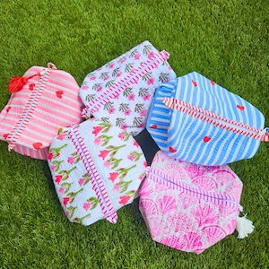 May include: Five quilted zippered pouches in various patterns and colors. One is pink and white striped with red hearts, one white with pink floral prints, one blue and white striped with red hearts, one white with pink tulips, and one pink with shells.