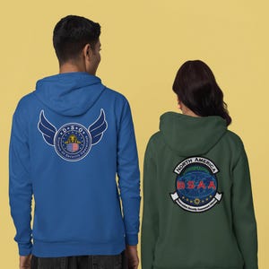May include: Two hooded sweatshirts, one blue and one green, with embroidered emblems on the back. The blue hoodie features a design with wings and the text "D.S.O. Division of Security Operations." The green hoodie displays a globe and the text "North America BSAA".