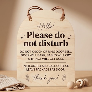 May include: Wooden sign with the text "Hello! Please do not disturb" in brown lettering. The sign has a curved top and a leather strap for hanging. The sign also includes the text "Do not knock or ring doorbell. Dogs will bark, babies will cry & things will get ugly."