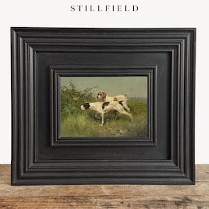 May include: A framed painting featuring two dogs in a field. The dogs are white with brown spots. The painting is set in a black wooden frame. The word "STILLFIELD" is at the top of the frame.