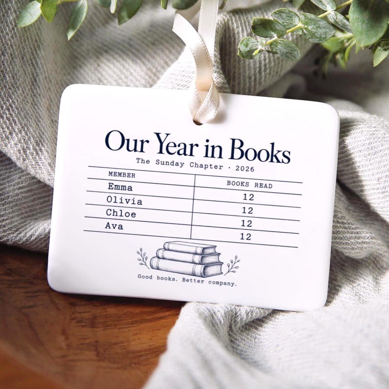 Peut inclure: Un ornement rectangulaire blanc en c&eacute;ramique avec un ruban cr&egrave;me, portant le texte noir Our Year in Books, The Sunday Chapter 2026, une liste de noms avec des nombres de livres, une illustration de trois livres et Good books. Better company.