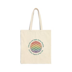 May include: Cream-colored tote bag with a rainbow-colored geometric design and the text "I Receive and Apply Divine Wisdom to Every Aspect of My Life." The bag has two handles and is made of a sturdy fabric.