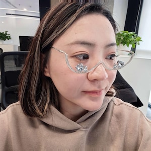 Può includere: Occhiali a mezza montatura color argento con un design decorativo e curvo. Le montature sono impreziosite da cristalli chiari e scintillanti. Gli occhiali hanno uno stile unico ed elegante.