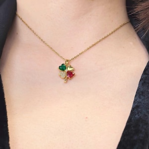 May include: A gold-colored necklace featuring a four-leaf clover pendant. Each leaf is a different color: green, red, yellow, and clear. The pendant is adorned with small, clear crystals. The necklace is worn around the neck.