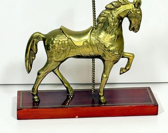 May include: A brass carousel horse figurine with intricate detailing, mounted on a rectangular, reddish-brown wooden base. The horse has a saddle and a decorative pole. The figurine is a decorative item.