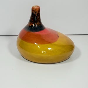 Peut inclure: Un vase en c&eacute;ramique avec un corps arrondi et un col &eacute;troit. Le vase pr&eacute;sente un d&eacute;grad&eacute; de couleurs, passant du jaune &agrave; la base &agrave; l'orange, au rose et au noir en haut. Le vase a une finition brillante.